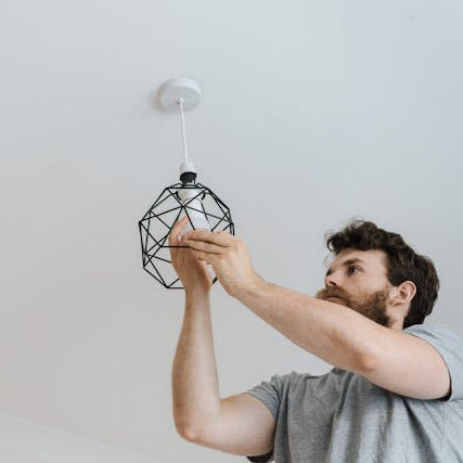 Electrician installing a modern ceiling light fixture during a residential electrical upgrade.