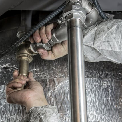Handyman using a red wrench to repair bathroom sink pipes during a plumbing service call.