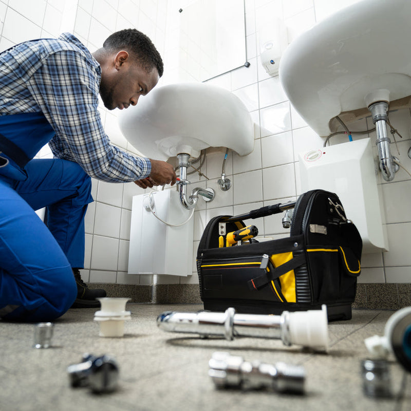 Skilled plumber in uniform repairing a bathroom sink drain with professional tools, offering reliable plumbing repair and installation for residential and commercial properties.