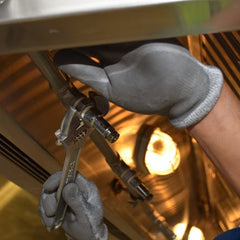 Worker wearing protective gloves tightening stainless steel plumbing pipes with a wrench.