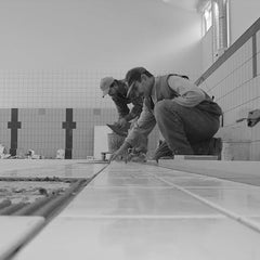 Contractors kneeling while installing ceramic floor tiles during home renovation in Brighton Colorado
